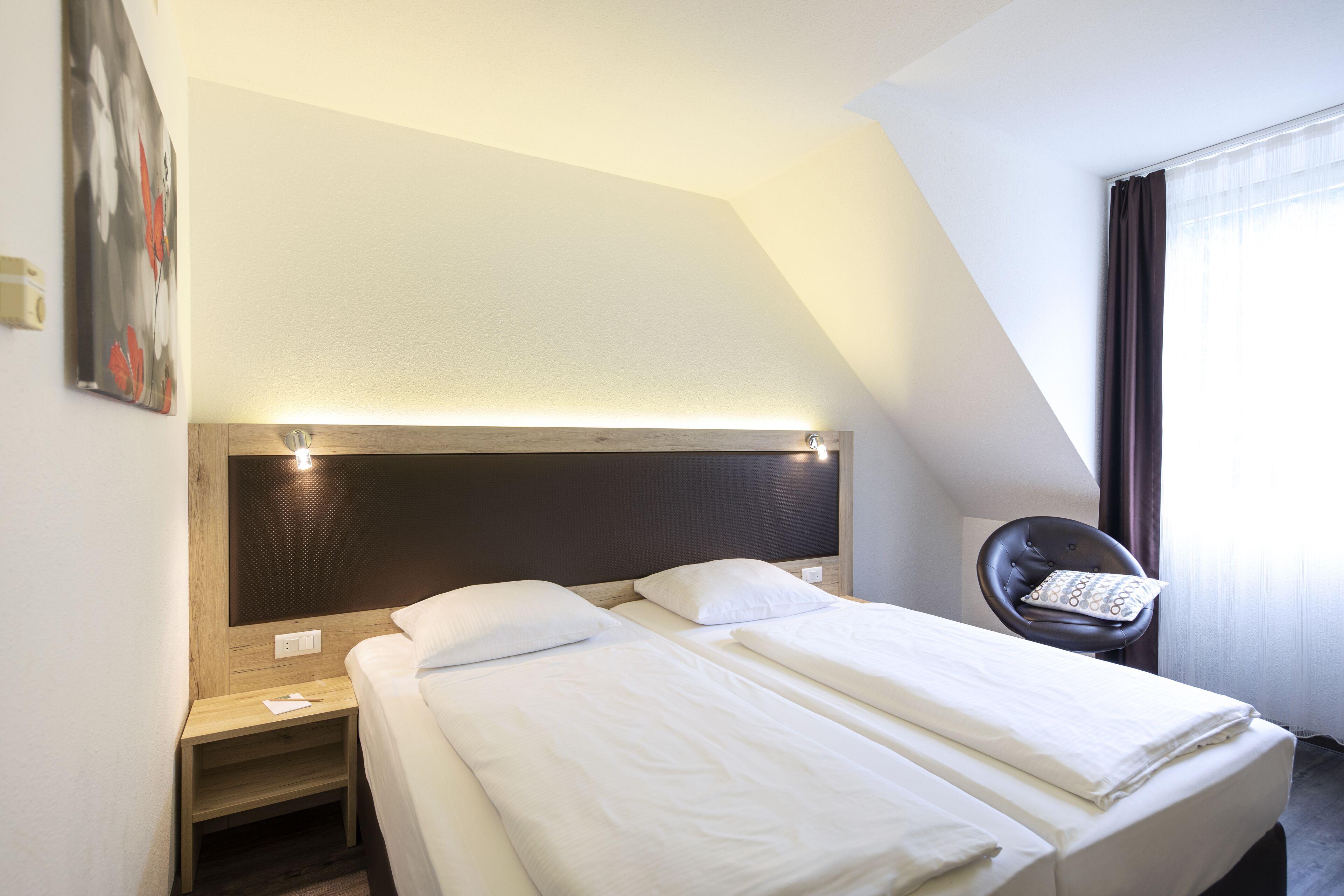 A hotel room with a bed, a chair, and a painting on the wall.