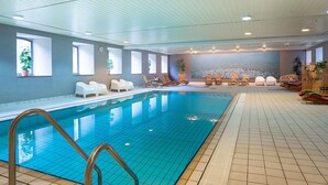 An indoor swimming pool with a tiled floor, a pool ladder, and several lounge chairs around the pool area. - ACHAT Hotel Monschau (Monschau)