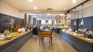A restaurant with a central serving counter, multiple tables, and a buffet area. - ACHAT Hotel Monschau (Monschau)