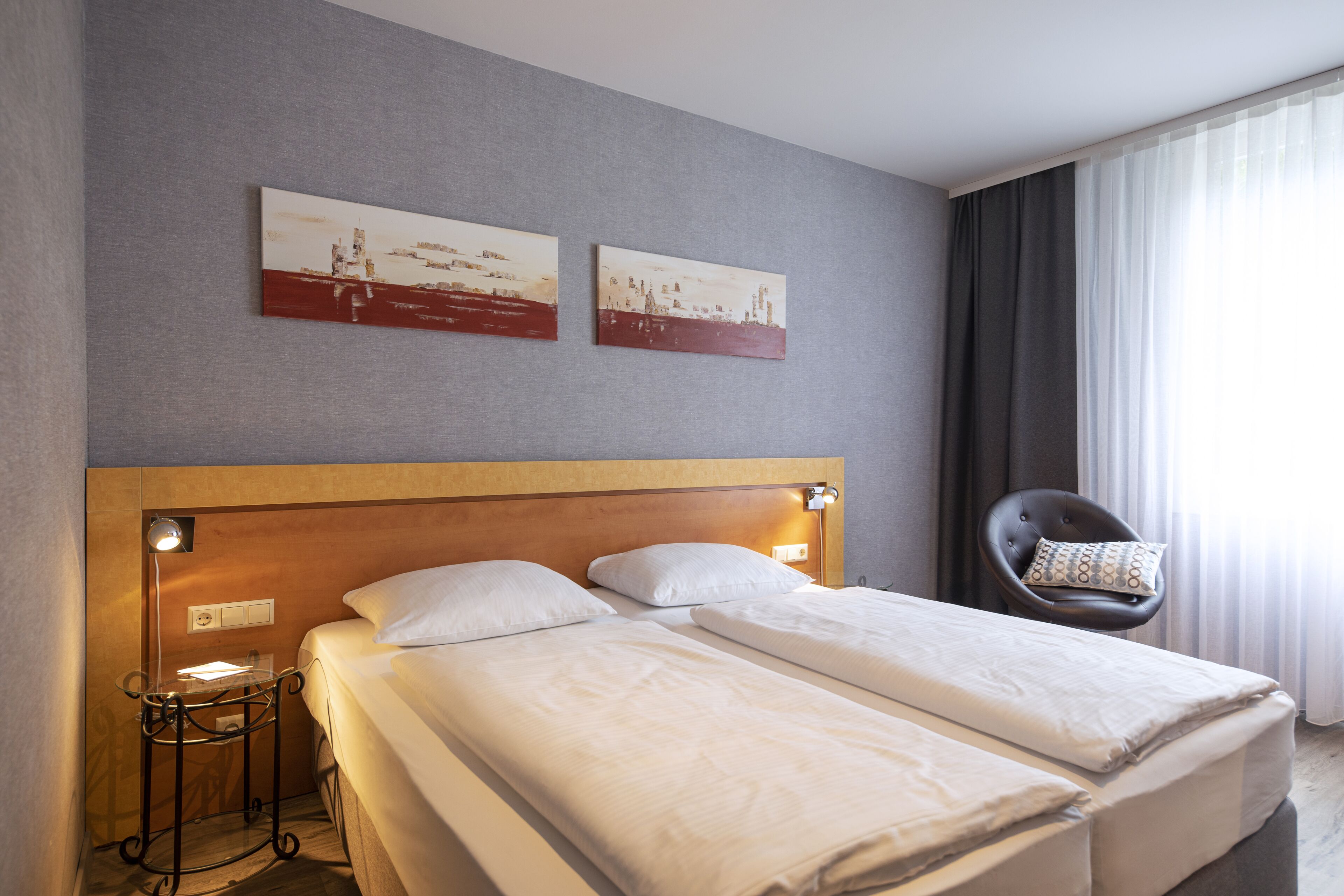 Ett hotellrum med två sängar, ett nattduksbord, en stol och två tavlor som hänger på väggen.