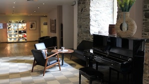 A lobby with a piano, seating area, and a display of items. - ACHAT Hotel Monschau (Monschau)