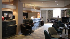 A hotel lobby with a reception desk, seating area, and a stone wall. - ACHAT Hotel Monschau (Monschau)