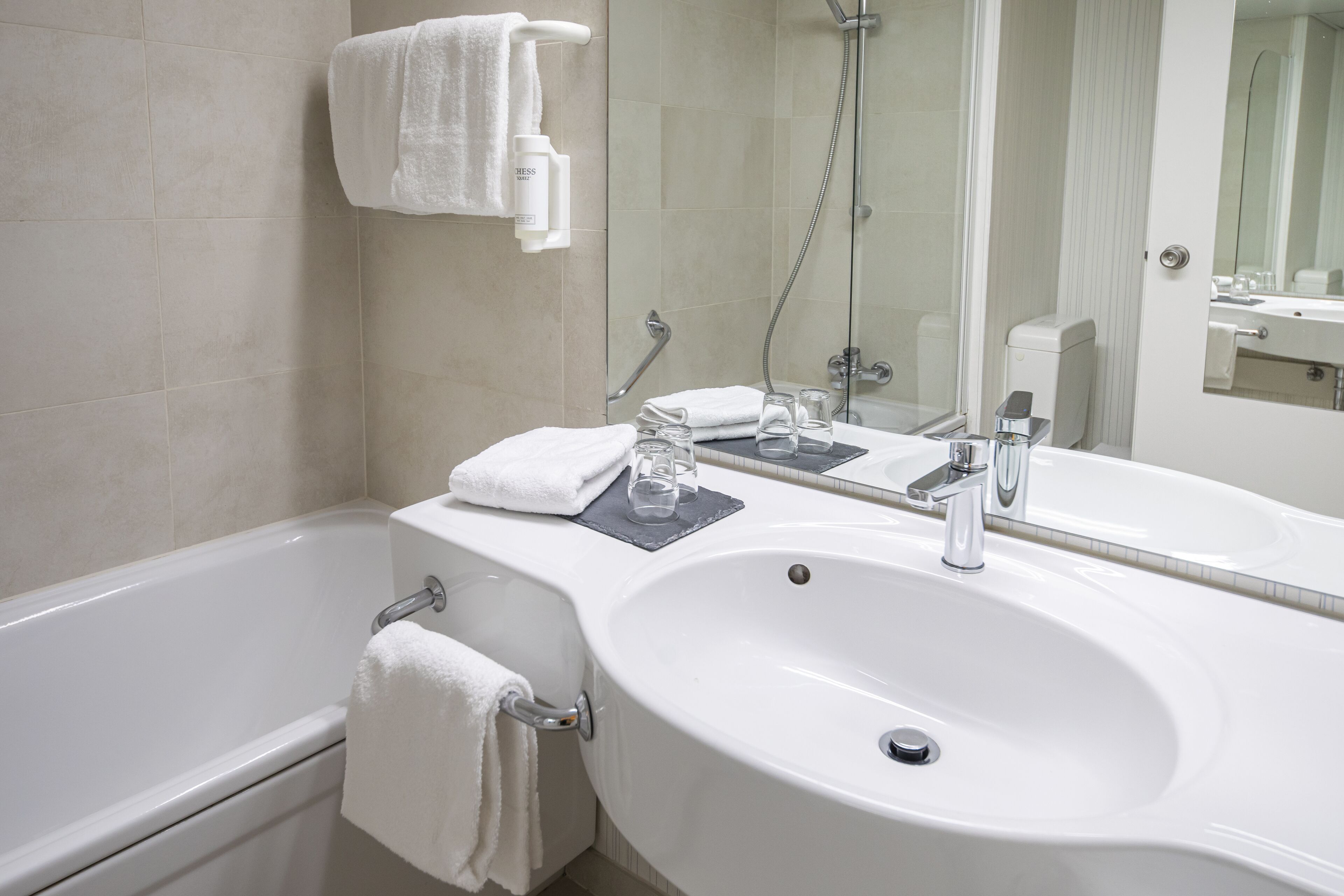 A modern bathroom with a white sink, a bathtub, and a large mirror.