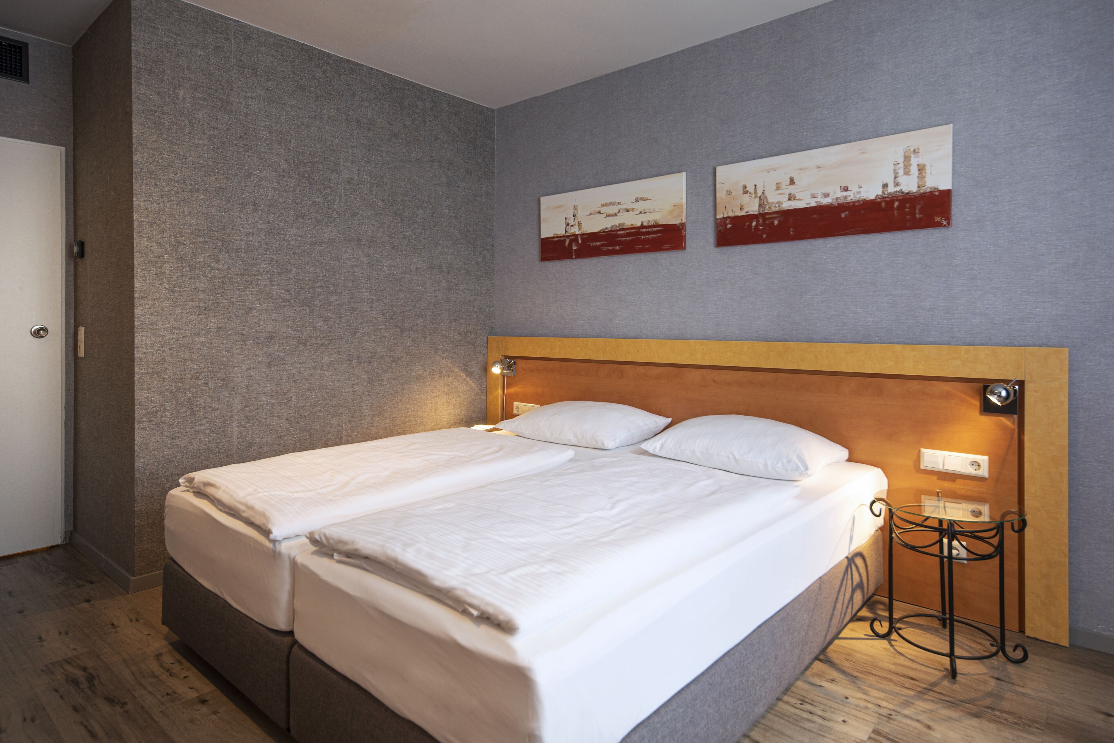 A double bed with a wooden headboard, a bedside table, and two wall-mounted artworks.