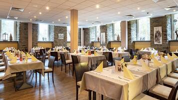 Ampia sala da pranzo con diversi tavoli apparecchiati per gli ospiti, caratterizzata da una parete in pietra e ampie finestre che lasciano entrare la luce naturale.