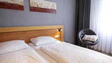 Une chambre d’hôtel avec deux lits simples, une tête de lit en bois, une chaise noire avec un coussin à motifs et deux tableaux accrochés au mur.