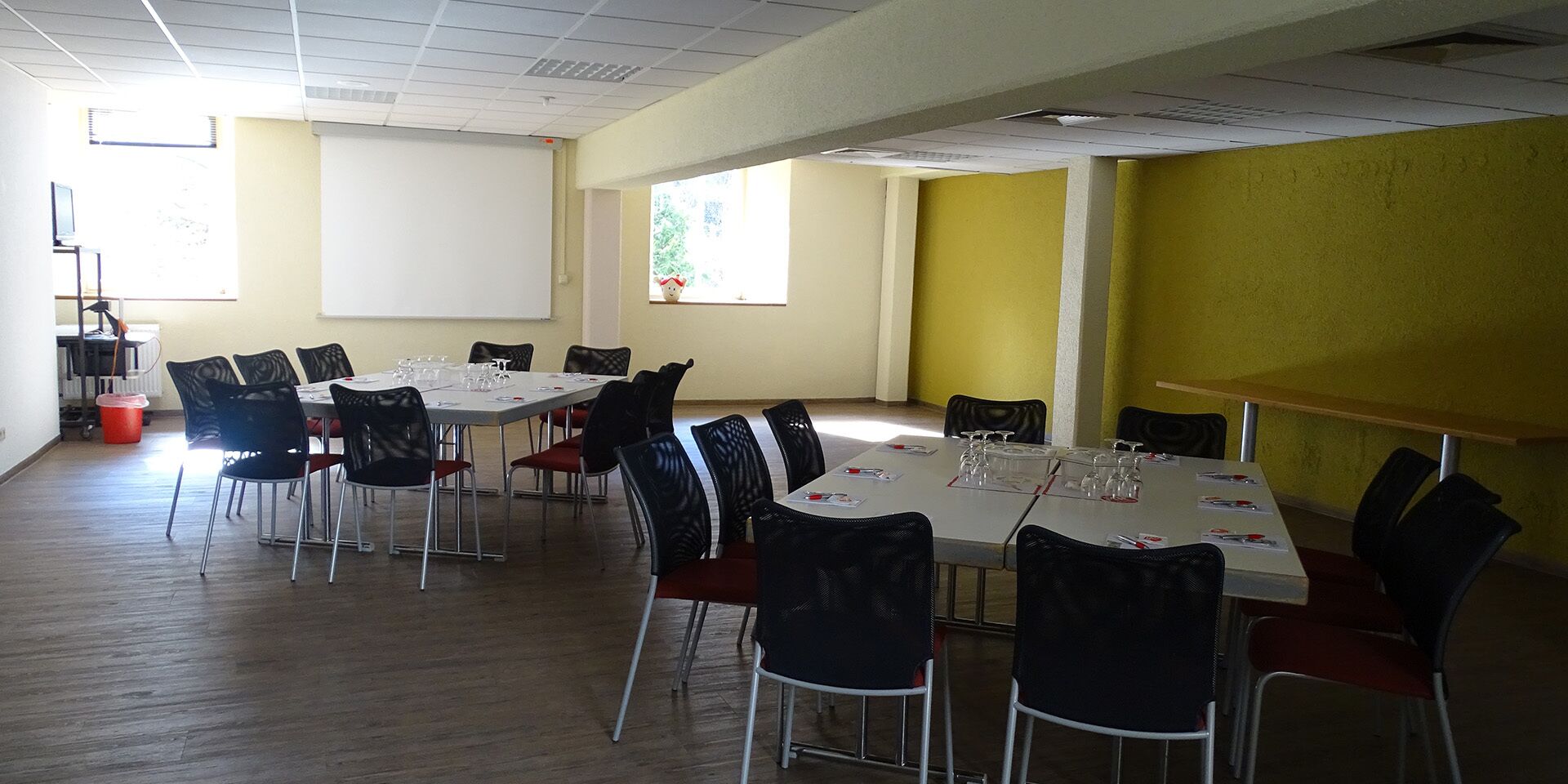 A conference room with a white table, black chairs, and a projector screen.
