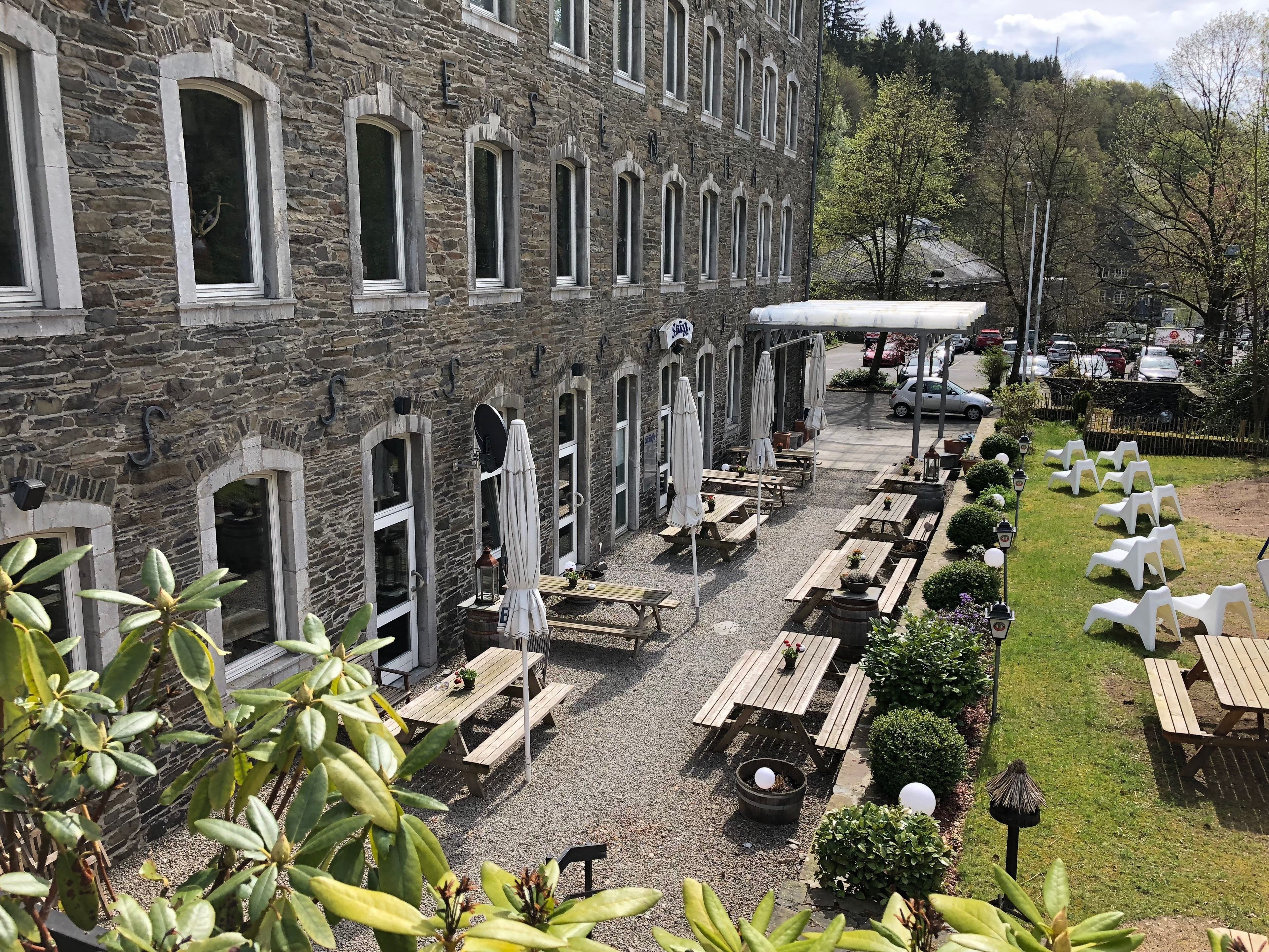 A stone building with multiple windows and outdoor seating areas with tables and umbrellas.