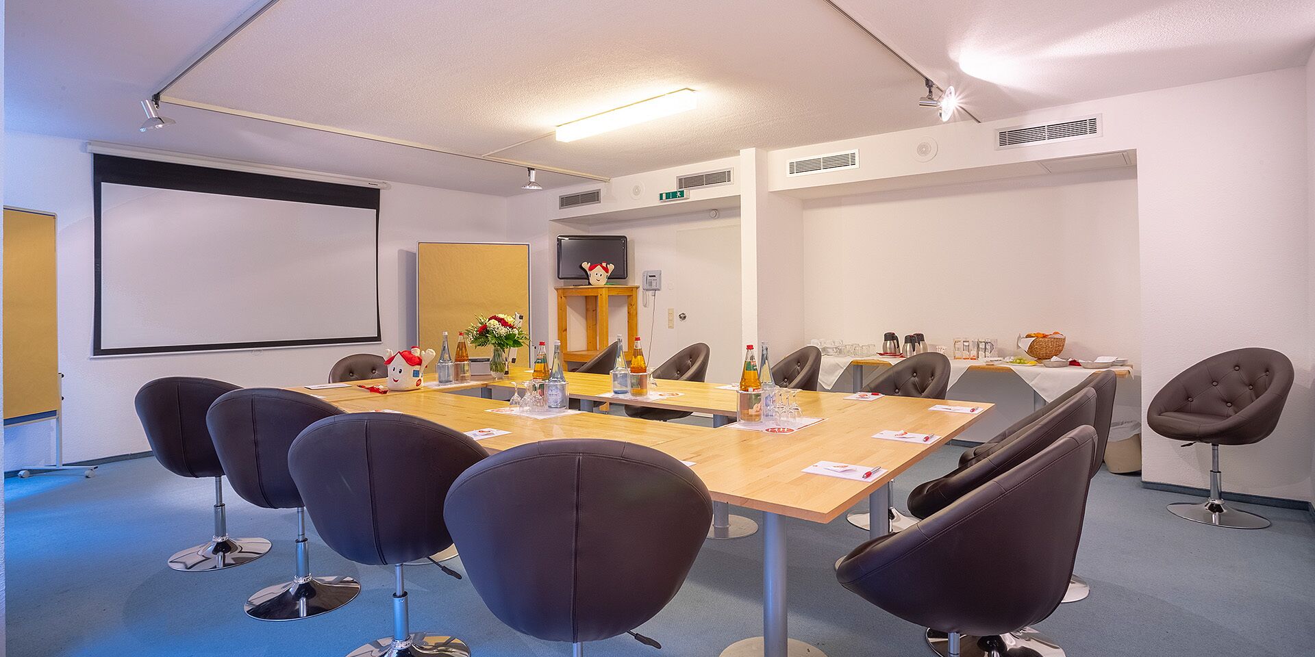 A conference room with a long table, several chairs, a projector screen, and a small stage area.