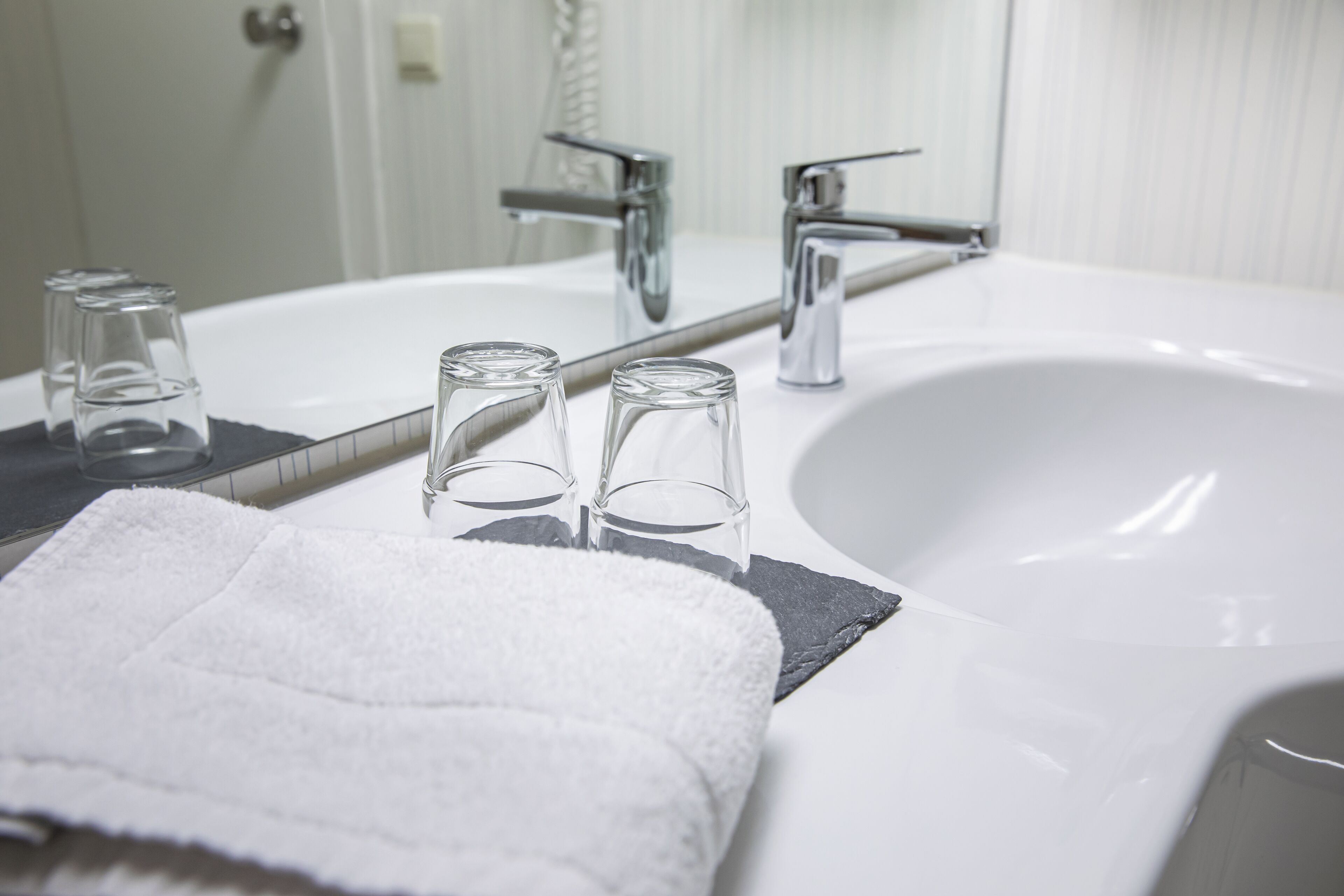 A bathroom with a white sink, two glass tumblers, and a white towel on a black mat.