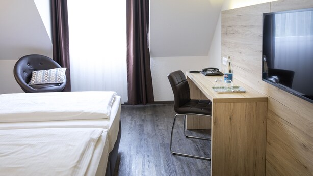 A hotel room with a bed, a desk with a chair, a television, and a window with curtains.