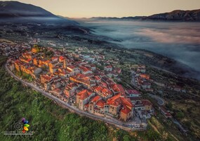 An aerial view of a town with a dense cluster of buildings, roads, and a surrounding mountainous landscape.