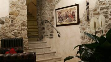 A stone-walled room with a staircase, a framed picture, a radiator, a leather sofa, and a potted plant.