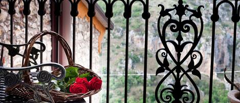 Un balcon orné d’un panier en osier contenant des roses rouges, d’une plante en pot et d’une rambarde en métal agrémentée d’éléments décoratifs.