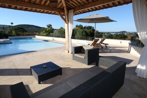 A poolside area with wicker furniture, a table, and an umbrella.