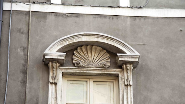 A building facade with a classical architectural style, featuring a symmetrical window with a decorative arch and a shell motif above it. - Relais San Lorenzo (Lucca)