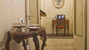 A hallway with a wooden table, a mirror, a framed picture, a small desk with a chair, and a patterned rug. - Relais San Lorenzo (Lucca)
