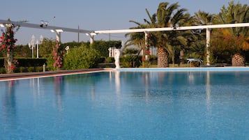 Relax by the serene pool surrounded by lush greenery and a shaded pergola.