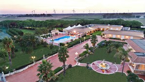 A large resort with a swimming pool, palm trees, and wind turbines in the background. - Agriturismo Al Parco (Lecce)