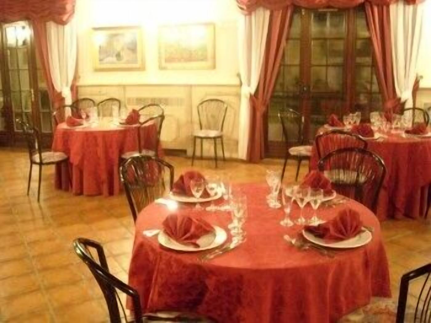 Un espace repas avec des tables rondes recouvertes de nappes rouges, chacune étant dressée avec des assiettes, des verres et des couverts.