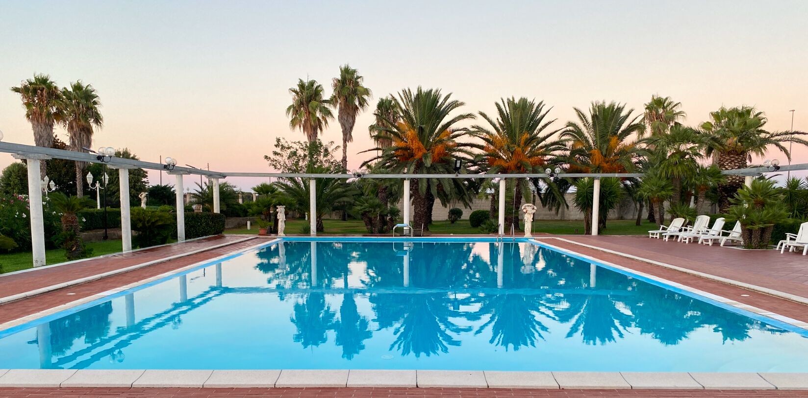 Una piscina rectangular con superficie de agua azul cristalina, rodeada por una estructura de pérgola blanca.