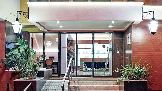 A hotel entrance with a glass door, a staircase, and potted plants. - Hotel Jardim (Aveiro)