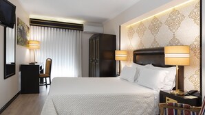 A hotel room with a large bed, a desk with a chair, a wardrobe, and a television. - Hotel Jardim (Aveiro)