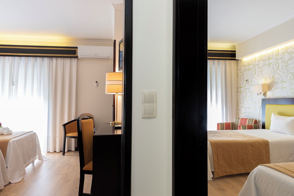 Une chambre d’hôtel avec deux lits, un bureau avec une chaise, une lampe et un climatiseur fixé au mur.