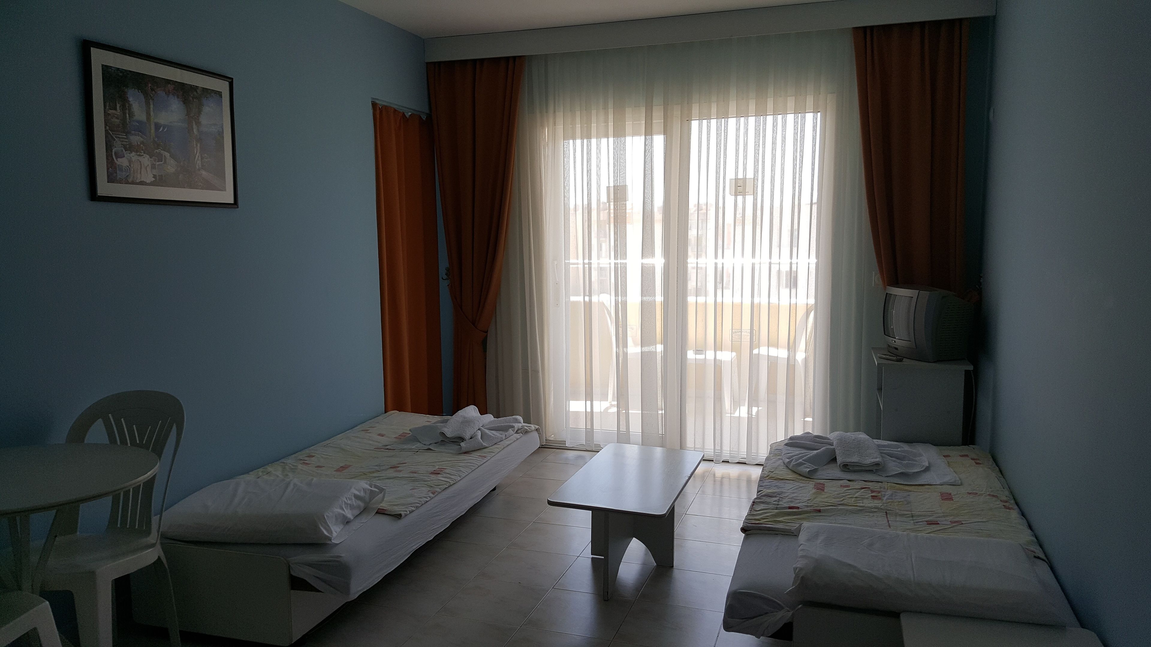 A room with two single beds, a small table, a TV, and a painting on the wall.