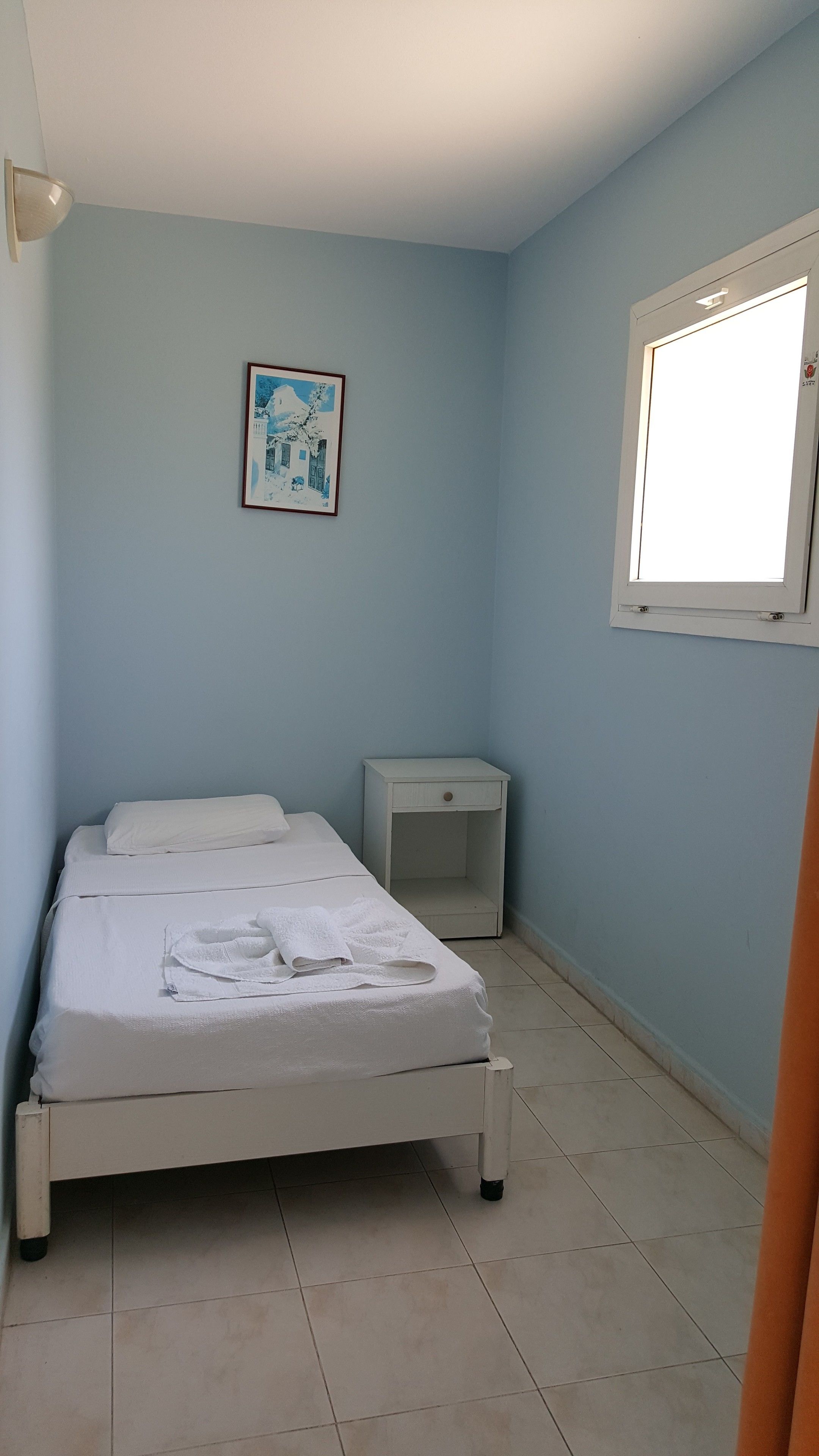 Une chambre à coucher avec un lit, une table de chevet, une fenêtre et un tableau accroché au mur.