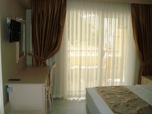 A hotel room with a bed, a desk, a chair, a television, and a window with curtains. - Golden Moon Apart Hotel (Kusadasi)