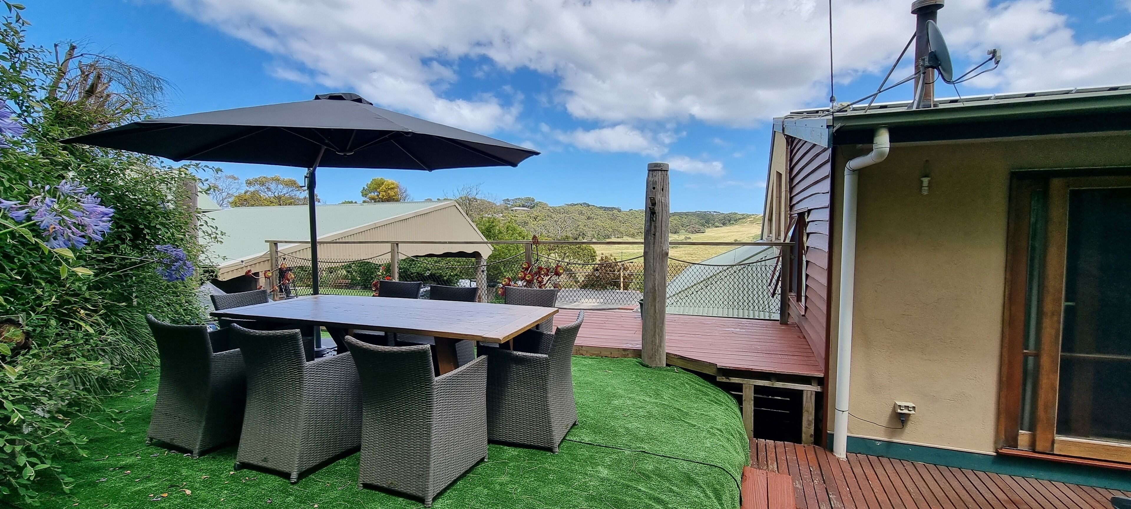 An outdoor patio with a table and chairs, surrounded by greenery and a view of the landscape.