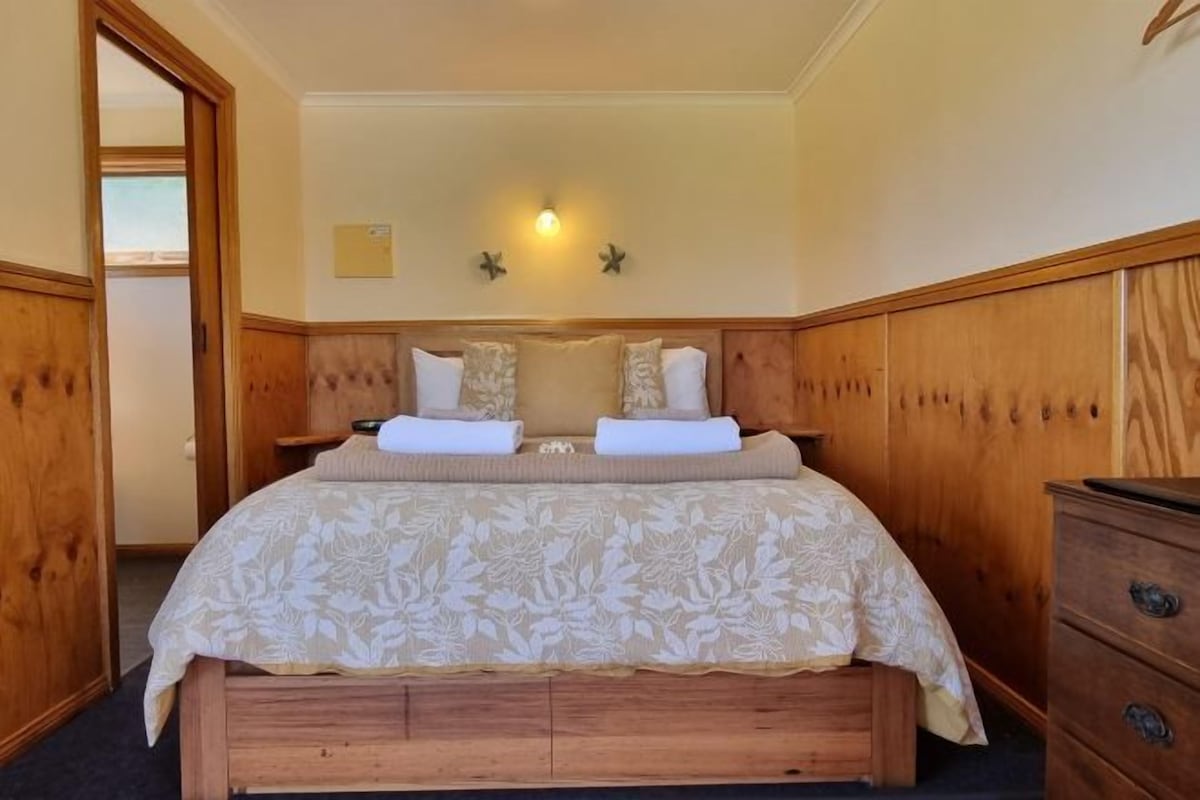 A bedroom with a wooden bed, two bedside tables, a nightstand, and a dresser.