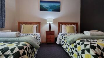 A room with two beds, each with a patterned bedspread and pillows, a nightstand with a lamp, and a painting on the wall.