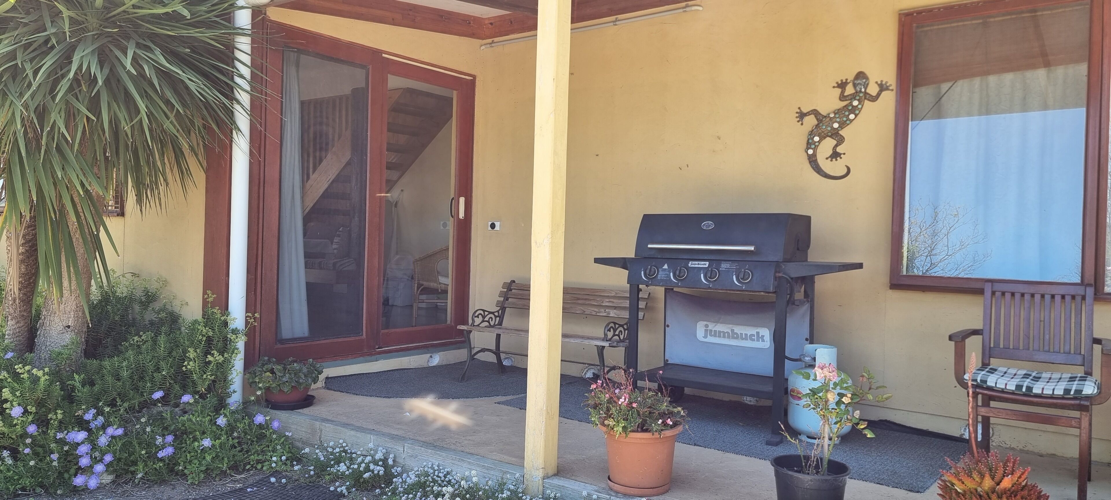 Une terrasse équipée d’un barbecue, de plantes en pot, d’un banc et d’une porte-fenêtre coulissante donnant sur un espace intérieur.