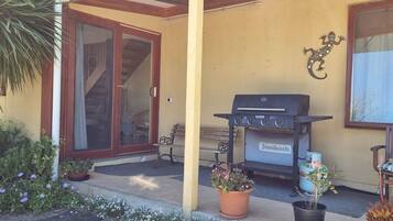Une terrasse équipée d’un barbecue, de plantes en pot, d’un banc et d’une porte-fenêtre coulissante donnant sur un espace intérieur.