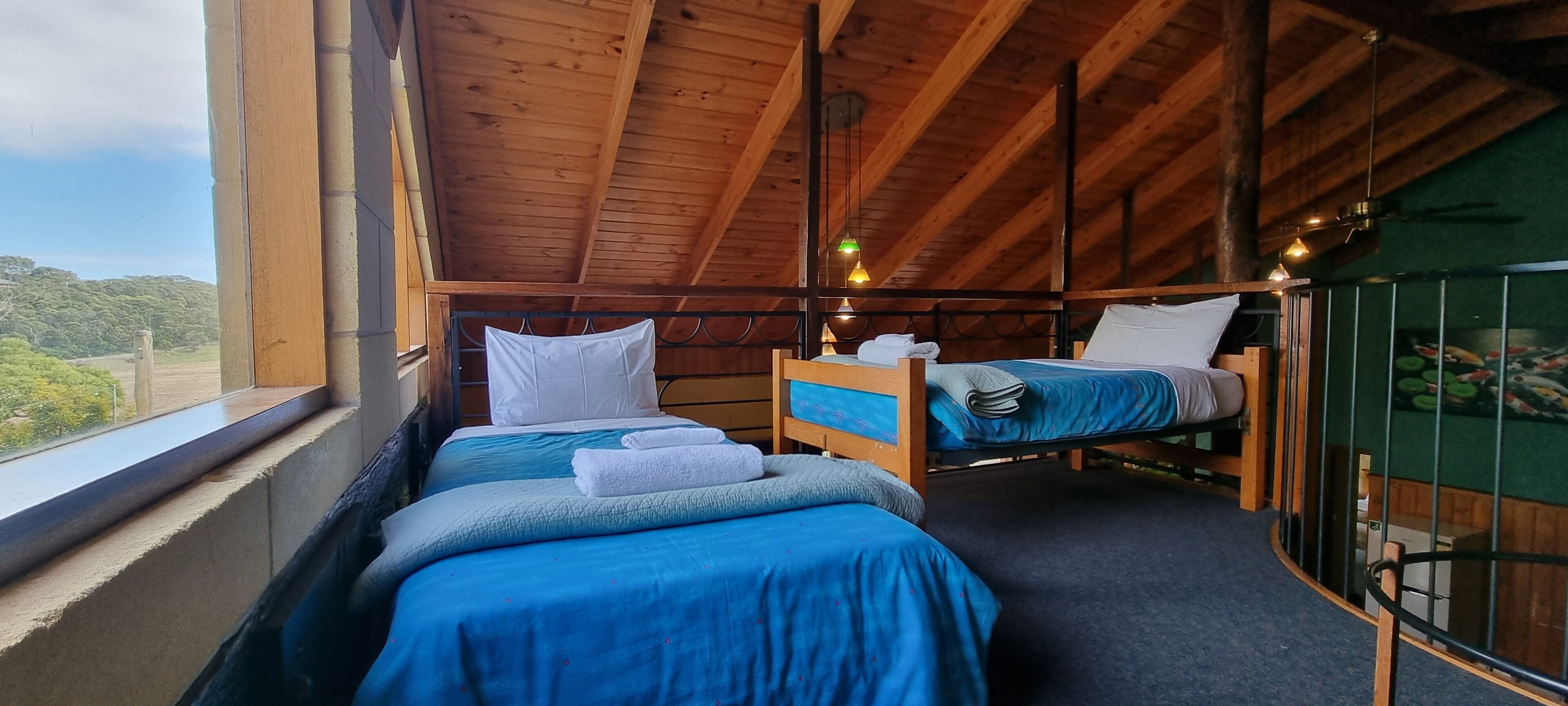 A room with two beds, wooden beams, a window with a view, and a green wall with a fish mural.