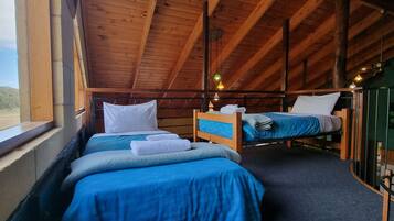 A room with two beds, wooden beams, a window with a view, and a green wall with a fish mural.