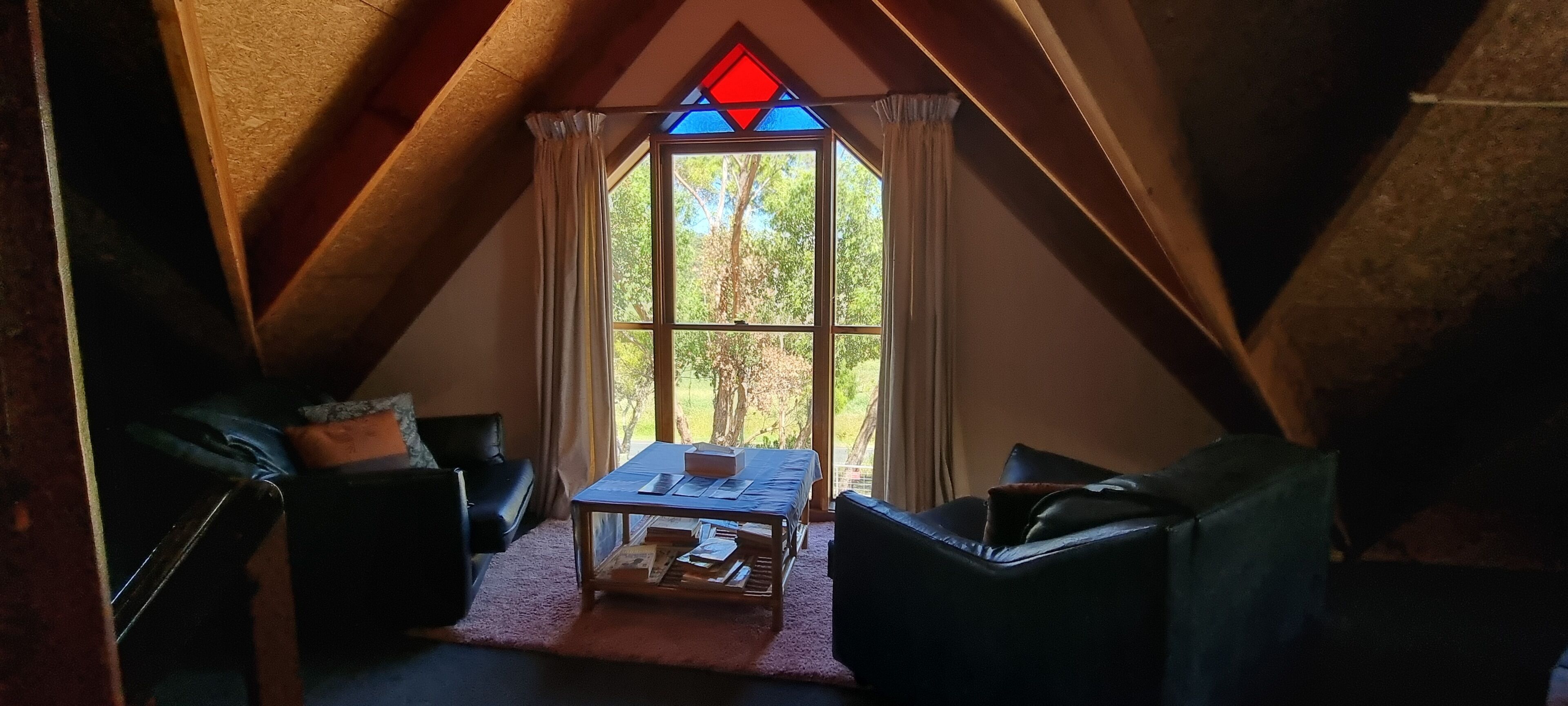 Une pièce mansardée agréable, avec une grande fenêtre, une table et deux chaises.