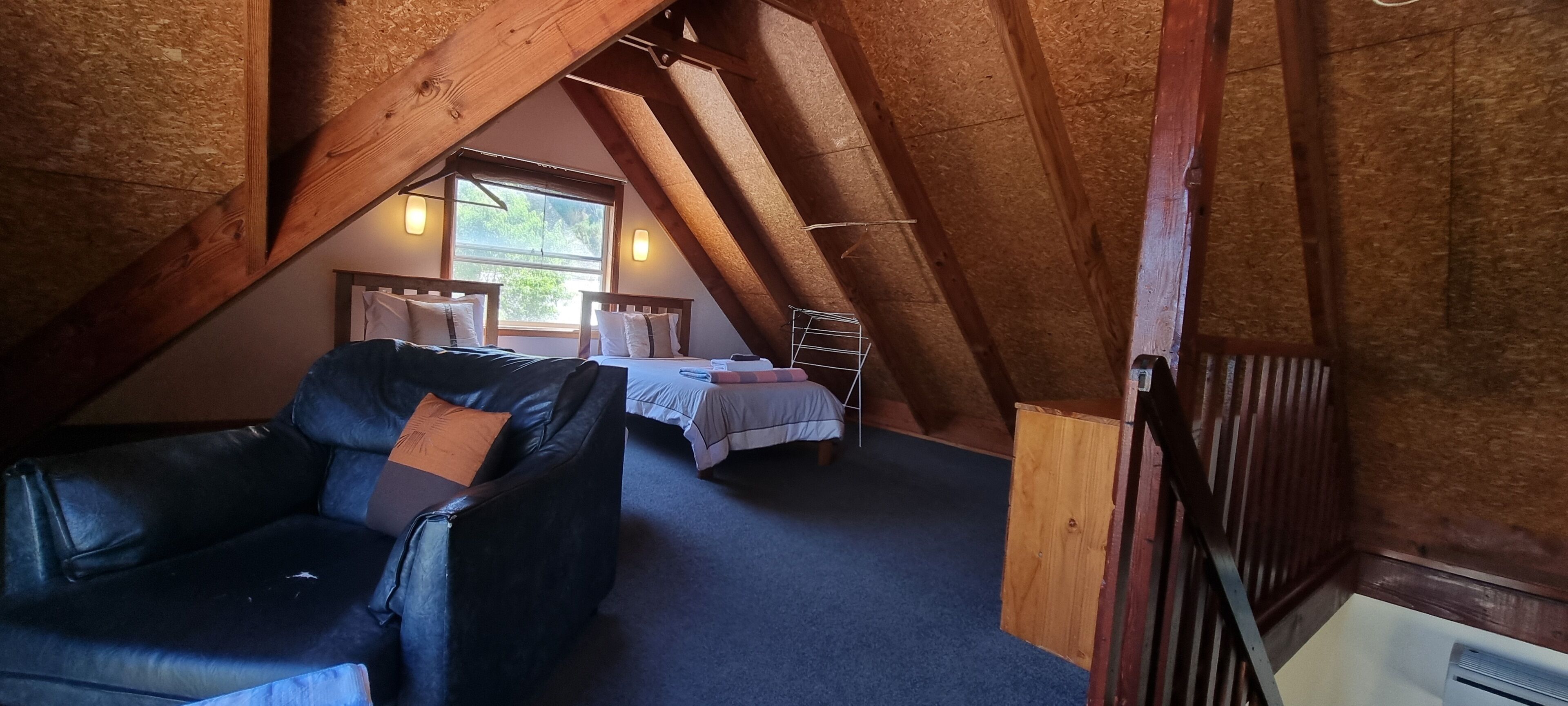 An attic bedroom with a loft bed, a leather chair, and a window providing natural light.