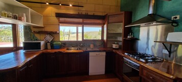 Una cocina con armarios de madera, horno empotrado, estufa a gas y ventana con vistas al exterior.