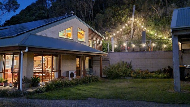 Une maison dotée d’un grand porche à l’avant, de panneaux solaires sur le toit et de guirlandes lumineuses dans le jardin.