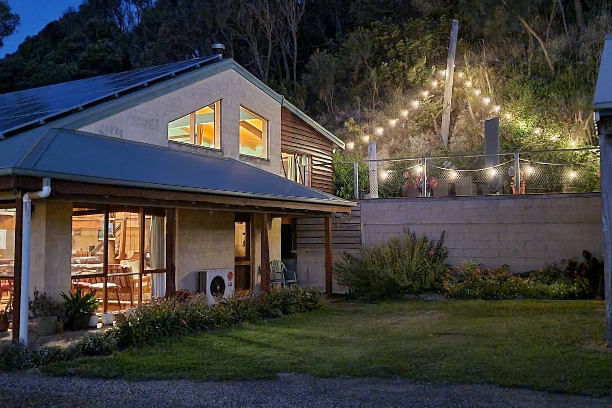A house with a large front porch, solar panels on the roof, and string lights in the backyard.