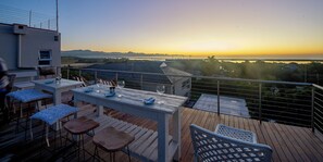 Una terraza con mesa y sillas, con vista a un paisaje pintoresco del atardecer y montañas lejanas.