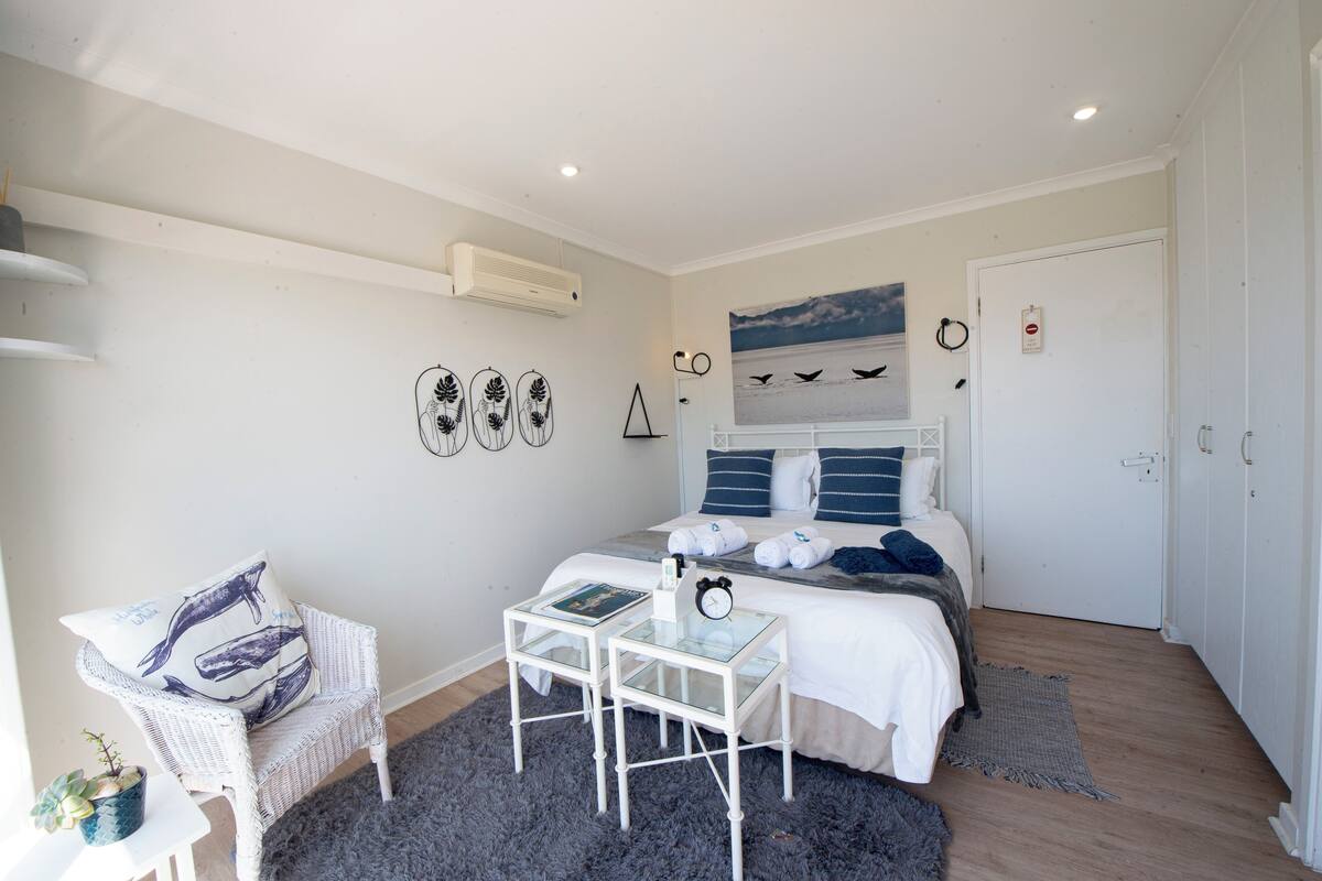 A bedroom with a bed, a chair, a small table, and a wall with decorative items.