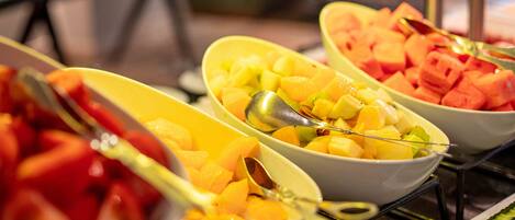 A buffet with various fruits and vegetables, including carrots, mangoes, and tomatoes.