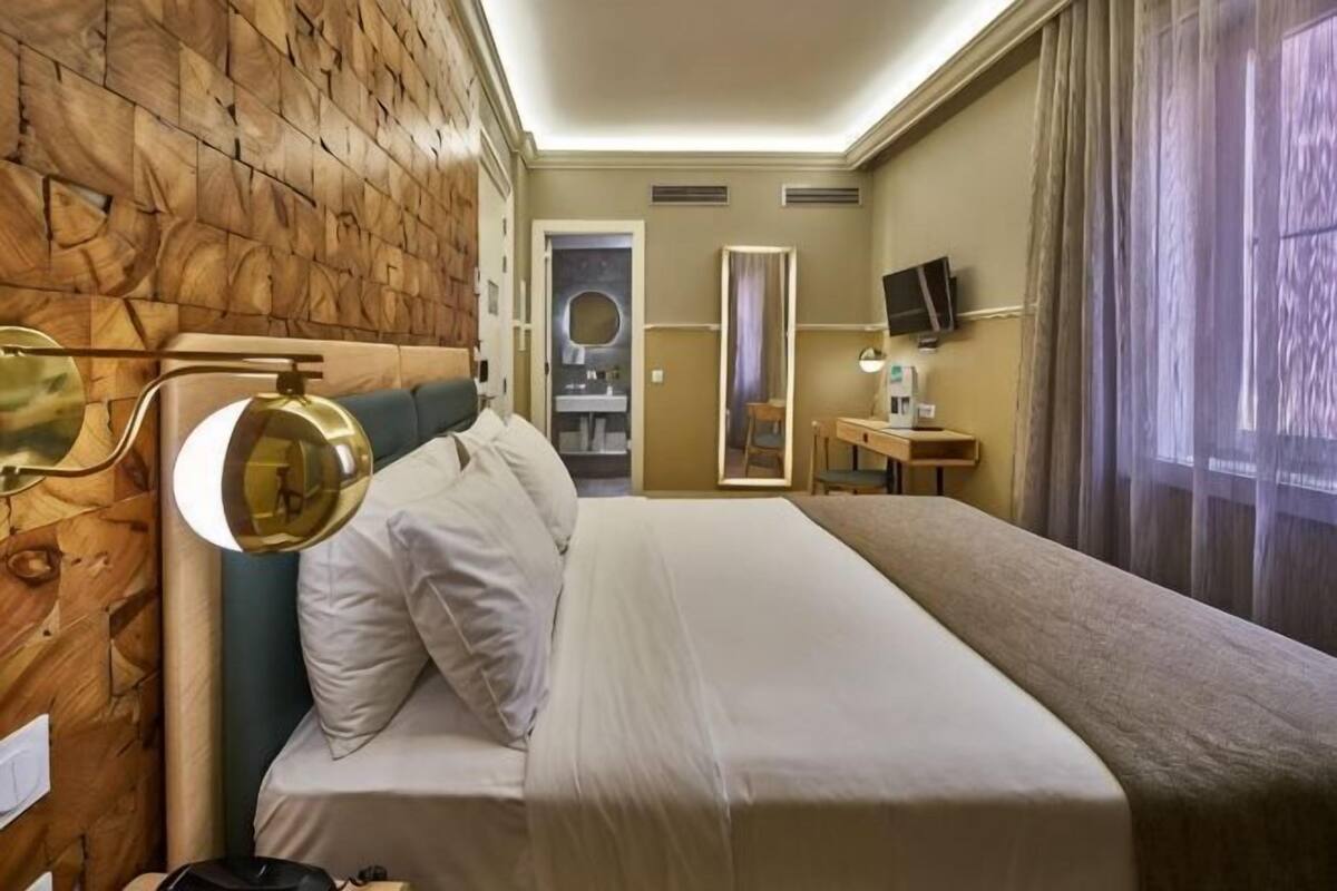 A hotel room with a bed, a mirror, a television, and a window with curtains.