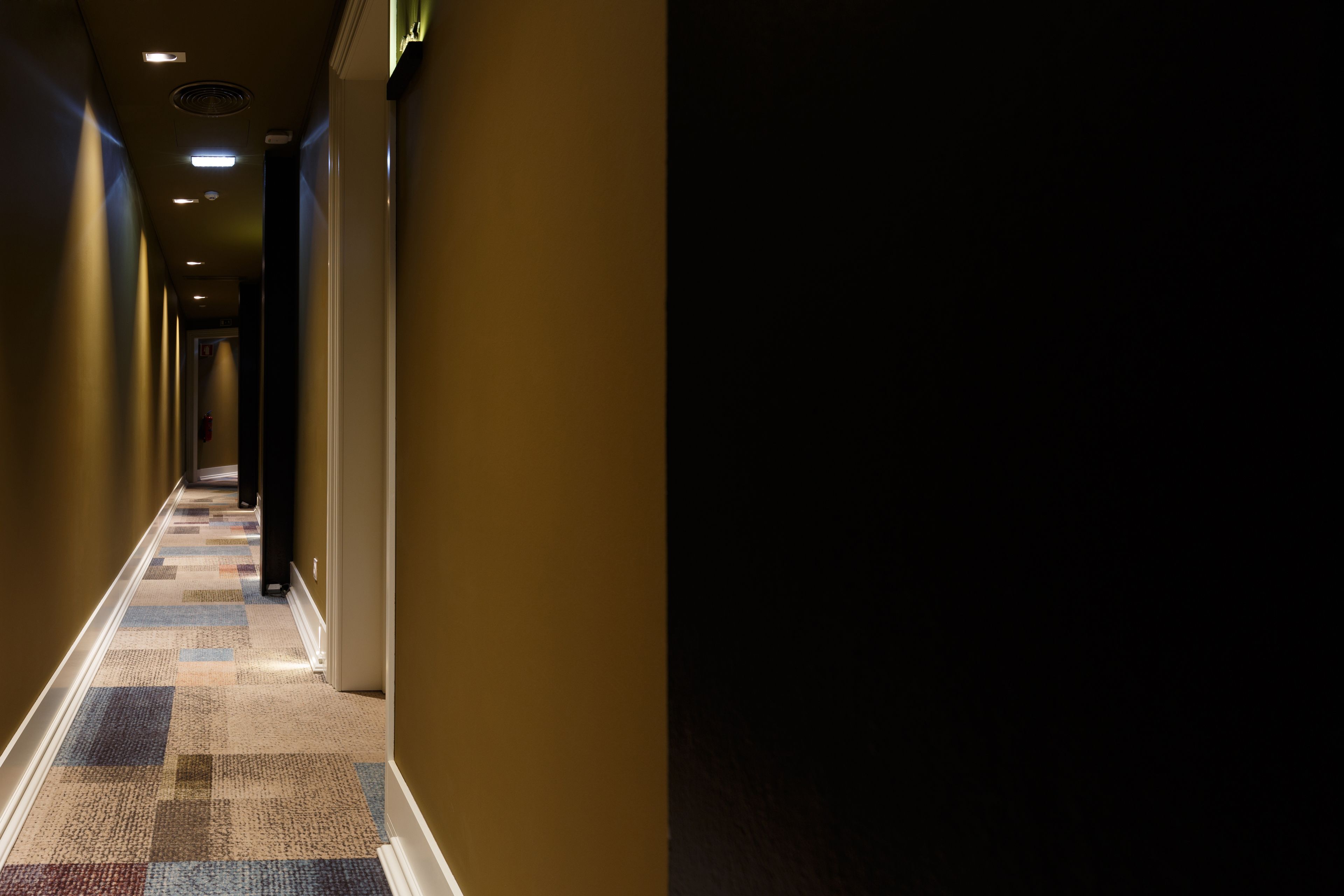 A long, narrow hotel corridor with patterned carpet and recessed lighting.