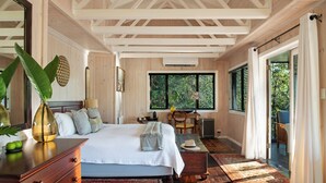 Un dormitorio espacioso con una cama grande, vigas de madera en el techo, vistas a través de la ventana y suelo de madera.
