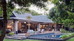 Una casa moderna con un porche cubierto, piscina y abundante vegetación.